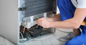 Technician repairing the compressor and coil system at the back of a commercial refrigerator.