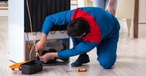 Professional freezer repair technician working on condenser and compressor components.